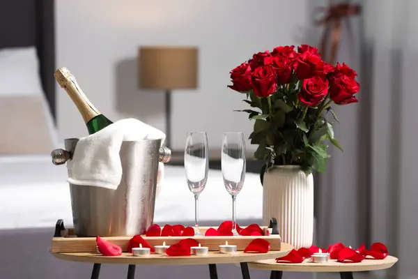 Honeymoon. Sparkling wine, glasses and bouquet of roses on wooden table in room