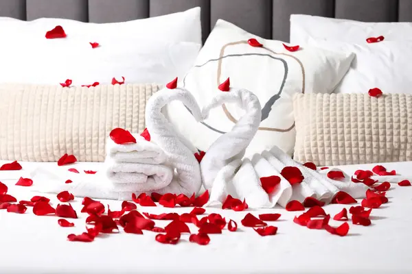Flitterwochen Schwäne Mit Handtüchern Und Schönen Rosenblättern Auf Dem Bett lizenzfreie Stockfotos