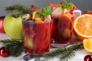 Aromatik Sangria içeceği bardaklarda, malzemelerde ve beyaz mermer masada Noel dekorunda.