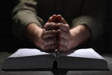 Din. Hıristiyan adam masada İncil için dua ediyor, yakın plan.
