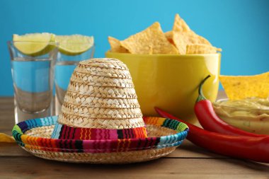Meksika şapkası, tekila, acı biber, cips ve açık mavi arka planda, ahşap masada guacamole.