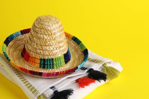 Mexican sombrero hat and poncho on yellow background, space for text