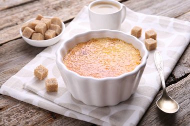 Lezzetli creme brulee kasede, şeker küpleri ve kaşık ahşap masada, yakın plan