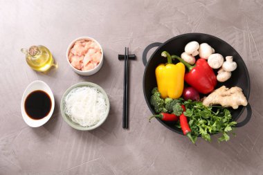 Wok, yemek çubukları ve gri desenli masa üzerinde farklı ürünler, düz yatak