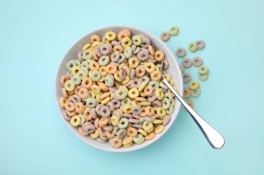 Lezzetli mısır gevreği halkaları kasede ve kaşıklar açık mavi masada, üst tarafta.