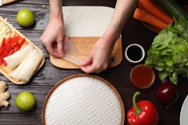 Lezzetli börek yapıyorum. Tahta masada taze sebzeleri pirinç kağıdına saran bir kadın.