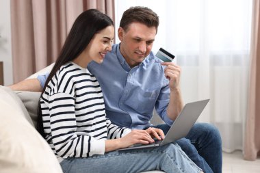 Bilgisayarlı ve kredi kartlı mutlu çift evde online alışveriş yapıyor.