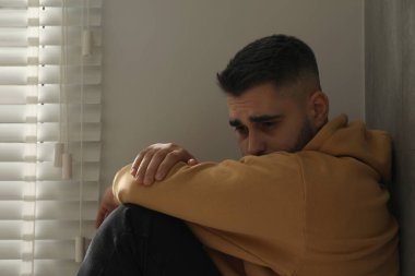 Evdeki pencerenin yanında oturan üzgün adam.