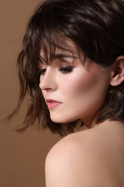 Kahverengi arka planda dalgalı saç stili olan güzel bir genç kadının portresi.