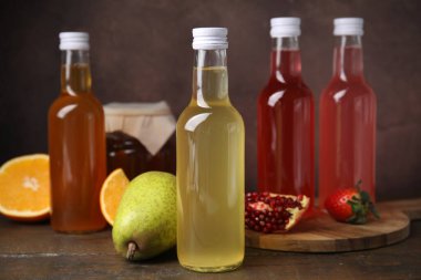 Delicious kombucha in glass bottles, jar and fresh fruits on wooden table clipart