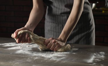 Ekmek yapıyorum. Ahşap masada hamur yoğuran kadın, yakın plan.