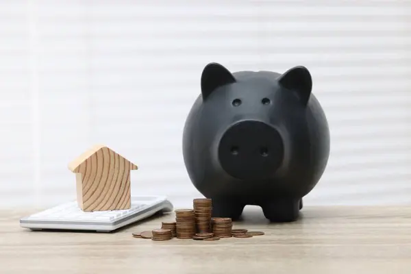 House model, calculator, piggy bank and stacked coins on wooden table