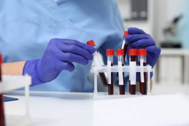 Laboratuvar testi. Kapalı alandaki beyaz masada tüplerde kan örnekleri olan bir doktor.