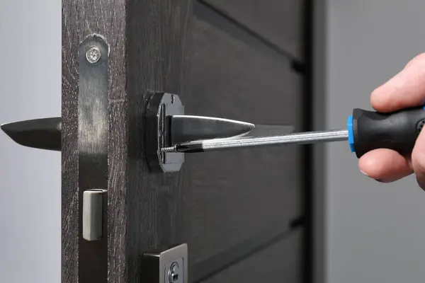 Handyman with screwdriver repairing door handle indoors, closeup