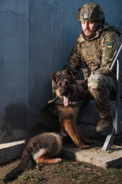 Alman çoban köpeği olan Ukraynalı asker dışarıda oturuyor.