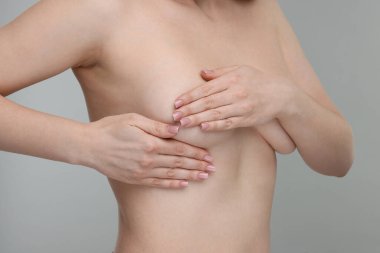 Mammoloji. Çıplak genç bir kadın açık gri arka planda göğüs muayenesi yapıyor. Yakın plan.