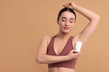 Güzel bir kadın bej arkaplan üzerine deodorant sürüyor, metin için boşluk