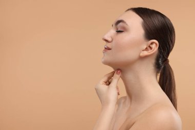 Güzel bir kadın bej arka planda çenesine dokunuyor. Metin için boşluk