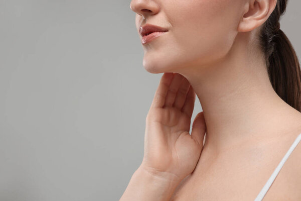 Женщина трогает шею на сером фоне, крупным планом. Пространство для текста