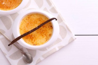 Lezzetli creme brulee kaseler, vanilya kapsülü ve kaşık beyaz ahşap masa, düz yatıyordu