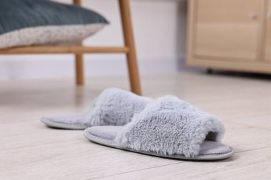 Açık ahşap zeminde gri yumuşak terlikler, yakın plan.