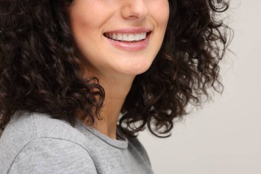 Açık gri arka planda diş beyazlatma şeridi kullanan genç bir kadın, yakın plan. Metin için boşluk