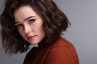 Gri arka planda dalgalı saç stili olan güzel bir genç kadın. Metin için boşluk