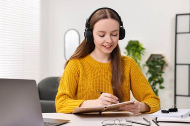 E-öğrenme. Beyaz masa içerisindeki online derste not alan genç bir kadın.