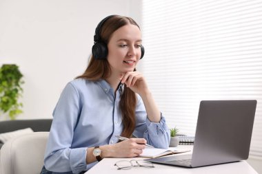 E-öğrenme. Beyaz masa içinde online ders sırasında dizüstü bilgisayar kullanan genç bir kadın.