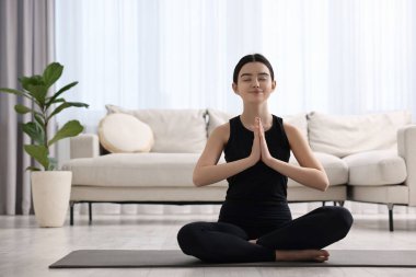 Evde yoga minderi üzerinde meditasyon yapan güzel bir kız.