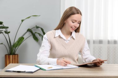 Ofisteki ahşap masada tablet kullanırken not alan kadın.