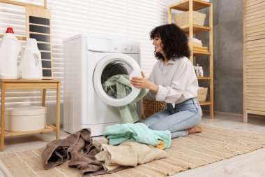 Çamaşır makinesine çamaşır koyan kadın.