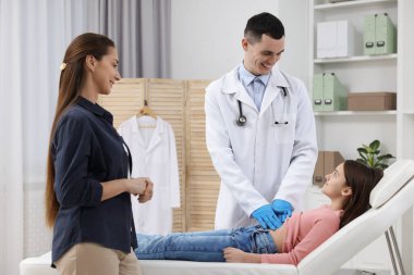 Gastroenterolog klinikteki kanepede karnı ağrıyan kızı muayene ediyor.