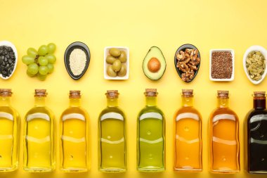 Vegetable fats. Different oils in glass bottles and ingredients on yellow table, flat lay clipart