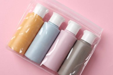 Pembe arka planda plastik poşet içinde kozmetik seyahat seti, üst manzara. Banyo aksesuarları