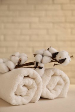 Yuvarlak havlu ve pamuk dalı beyaz masanın üzerinde, tuğla duvarın yanında, metin için yer var.