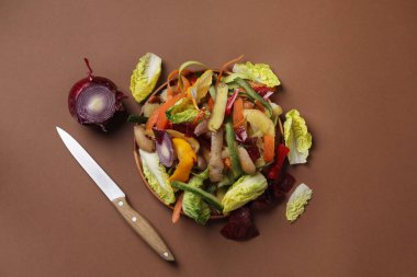 Kahverengi arka planda taze sebze ve bıçak kabukları, düz uzanmış.