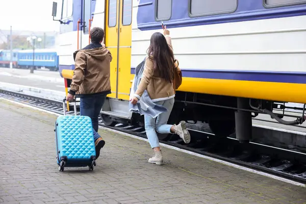Being late. Couple with suitcase running towards train at station, back view. Space for text