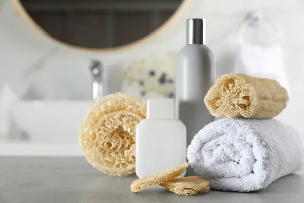 stock image Natural loofah sponges, towel and cosmetic products on table in bathroom. Space for text