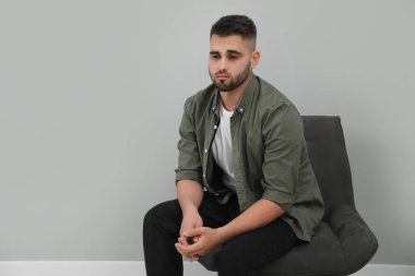 Üzgün adam açık gri duvarın yanında oturuyor. Metin için boşluk