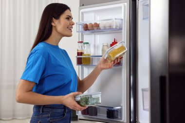 Buzdolabından sebzeli konteynırları çıkaran genç bir kadın.