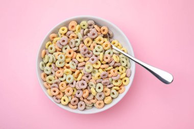 Lezzetli mısır gevreği halkaları kasede ve kaşık pembe masada, üst tarafta.