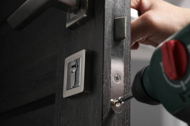 Elektrikli tornavidayla tamirci kapı kolunu içeride tamir ediyor, yakın plan.