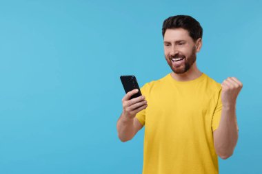 Açık mavi arka planda akıllı telefon kullanan mutlu bir adam. Metin için boşluk