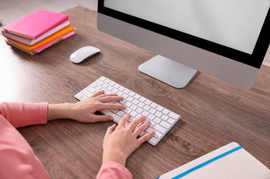 E-öğrenme. İçerideki masada çevrimiçi ders sırasında bilgisayar kullanan kız, yakın plan