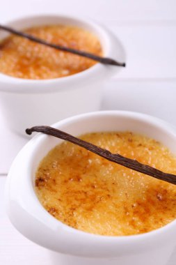 Lezzetli creme brulee kaseler ve beyaz masa üzerinde vanilya kabukları, yakın çekim