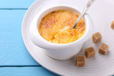 Açık mavi ahşap masada servis edilen kasedeki leziz creme brulee, yakın plan.