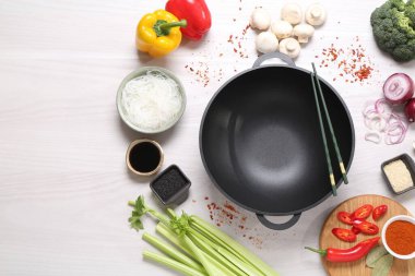 Wok, yemek çubukları ve beyaz ahşap masa üzerinde farklı ürünler, düz yatak. Metin için boşluk