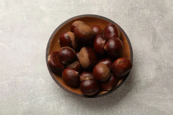 stock image Roasted edible sweet chestnuts in bowl on light grey table, top view