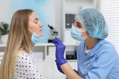 Laboratuvar testi. Doktor hastanedeki pamuklu bezle hastanın burnundan örnek alıyor.